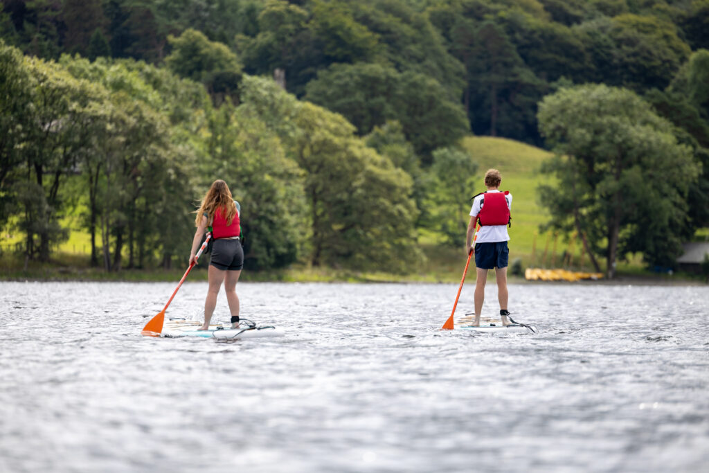 teen male and female paddle boarding away from camera on a sunny day at coniston water