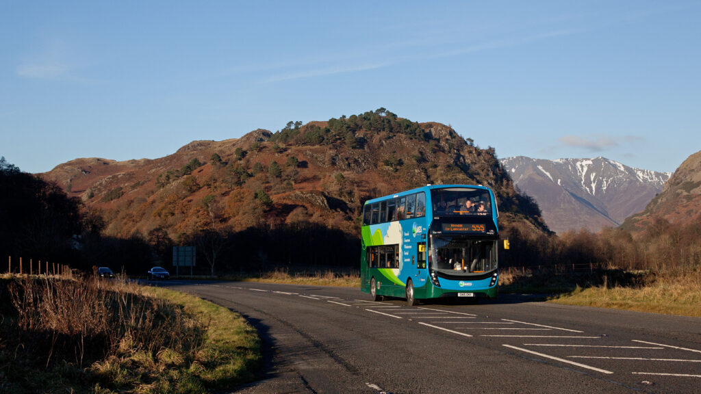 blue double decker 555 bus on road through brown fells