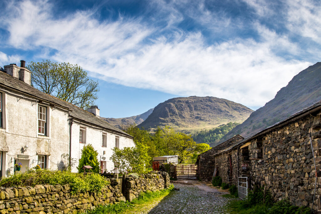 looking down single land street with rural houses on left and right, fell in backdrop