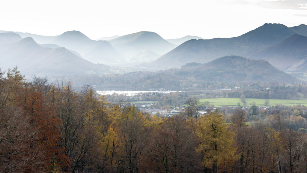 misty landscape view of borrowdale valley, backdrop fells, foreground autumnal woodland and keswick town