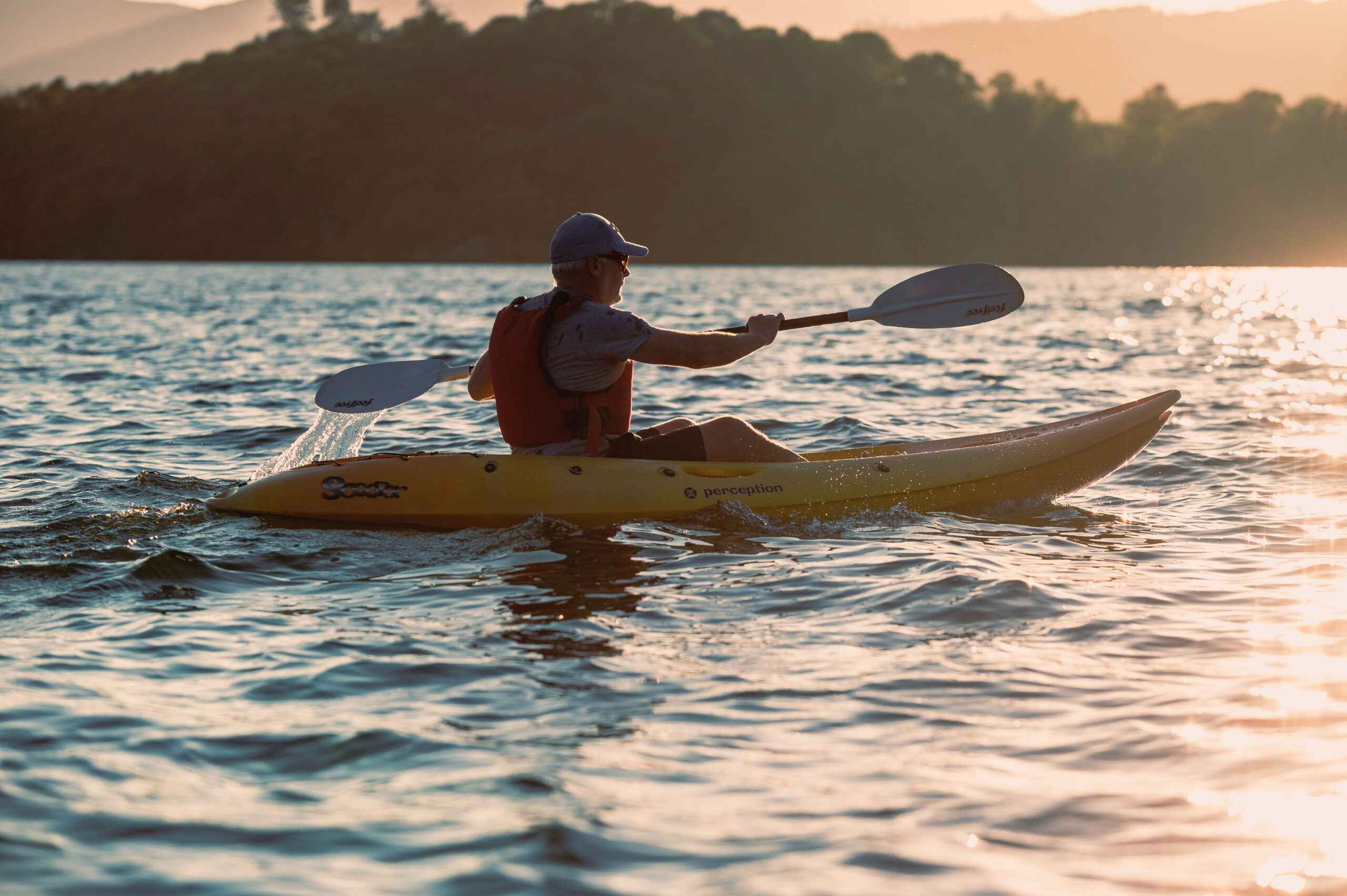 adult male in yellow kayak paddling on lake at sunset