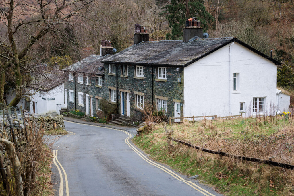 row of slate and white limewash houses to the right of a gently sloping single width road amongst brown and green vegetation