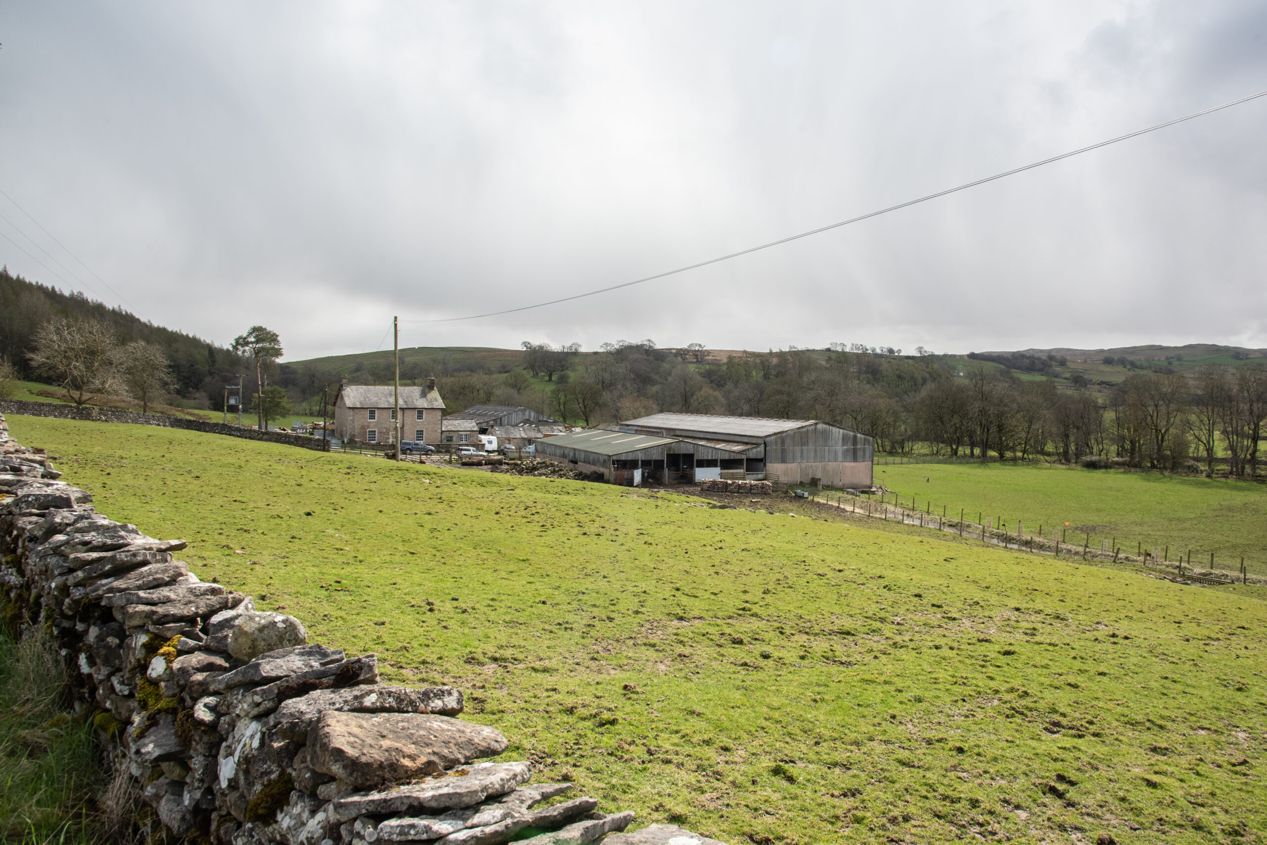 View over field towards farmhouse and farm buildings.