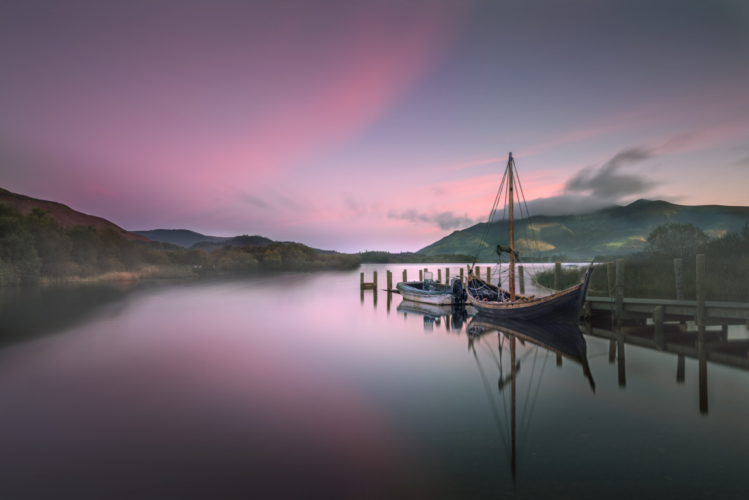 glassy derwent water with moored boats at a pink sunset
