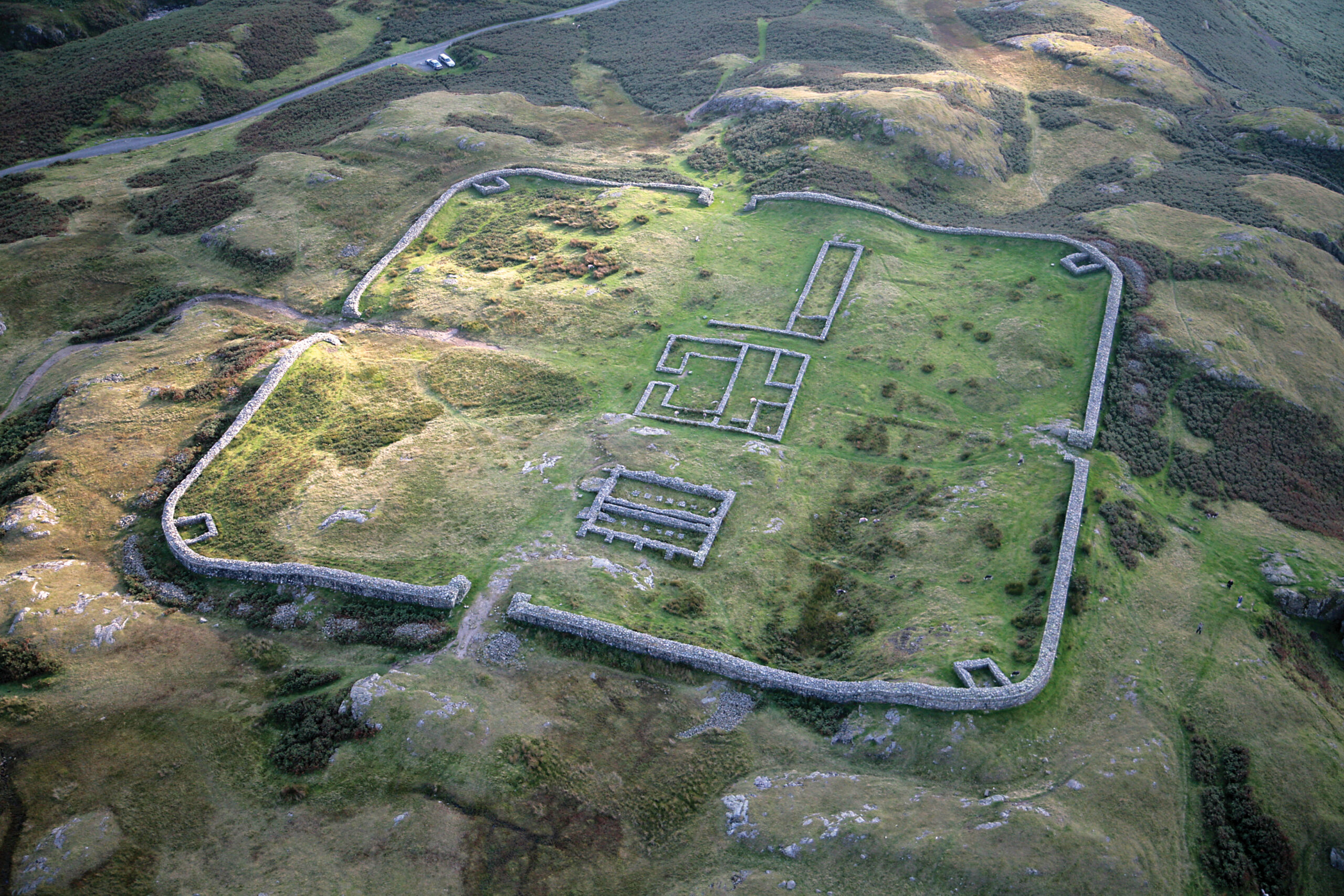 Aerial view of the ruins of a fort. You can see the square outline of the footprint of the fort, with the remains of some buildings within the square. The landscape outside the fort is a mix of light and dark brown