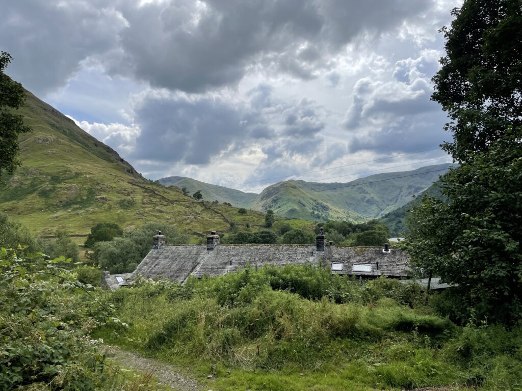 slate barn roof emerging from lush green vegetation in the valley bottom of surrounding fells