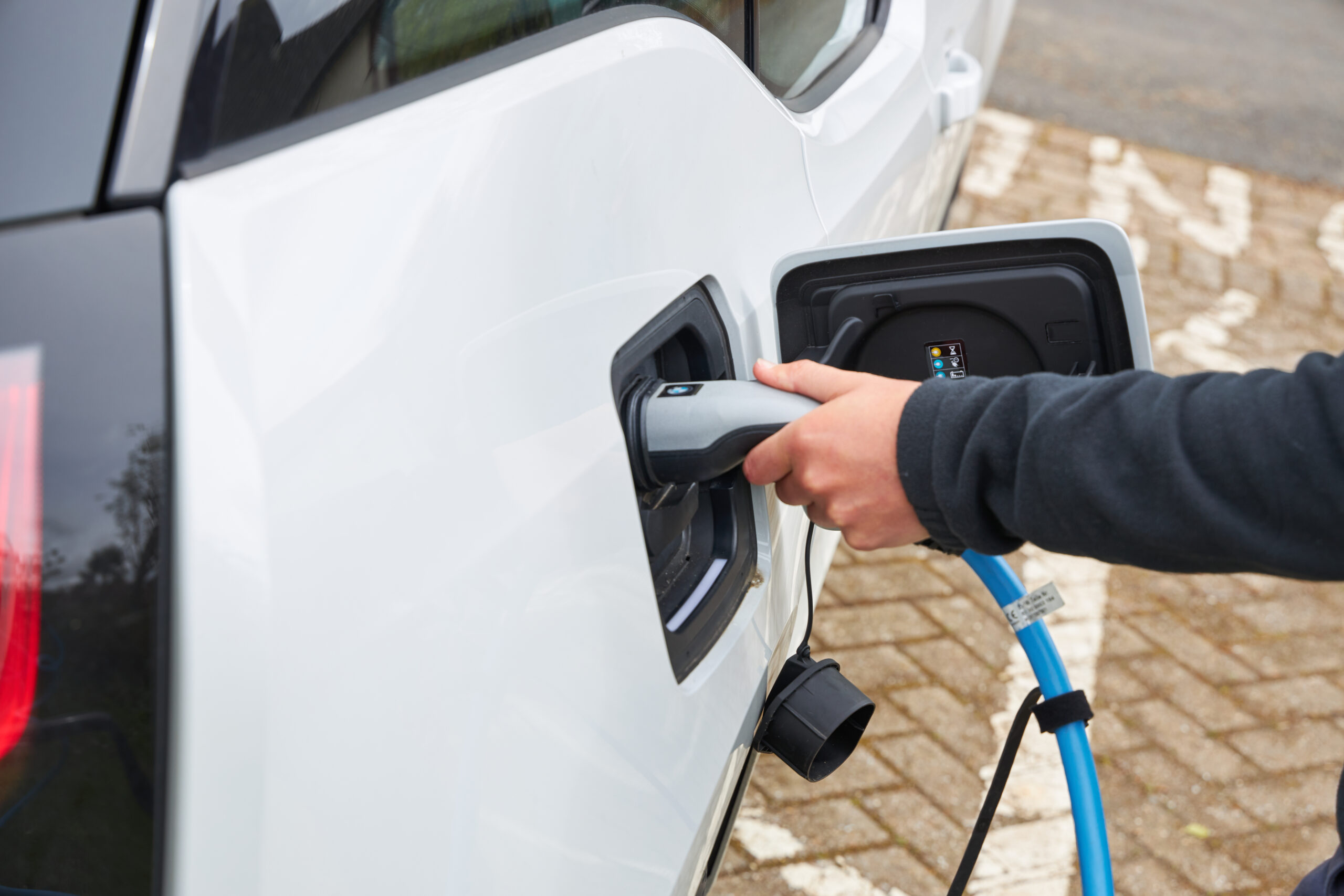 electric vehicle charging cable being plugged into white car