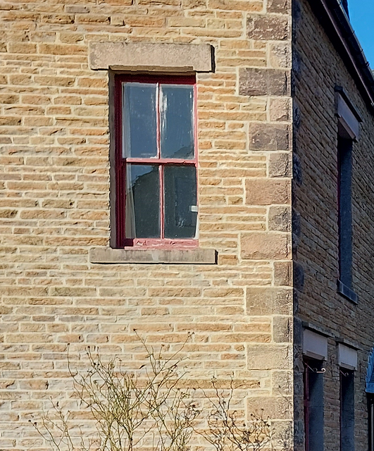 close up of house exterior walls made of light orange brown sandstone with small rectangle window