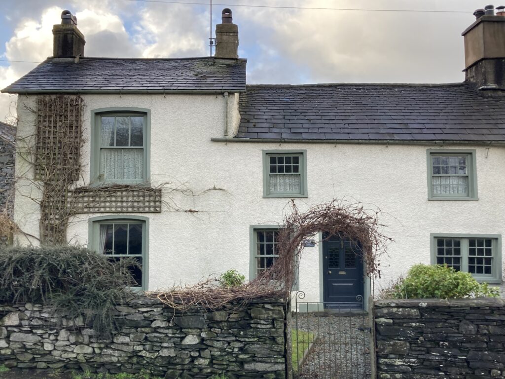 two white roughcast render semi-detached houses with duck egg wood window frames, slate roofs, climbing plants and a dry stone wall in front