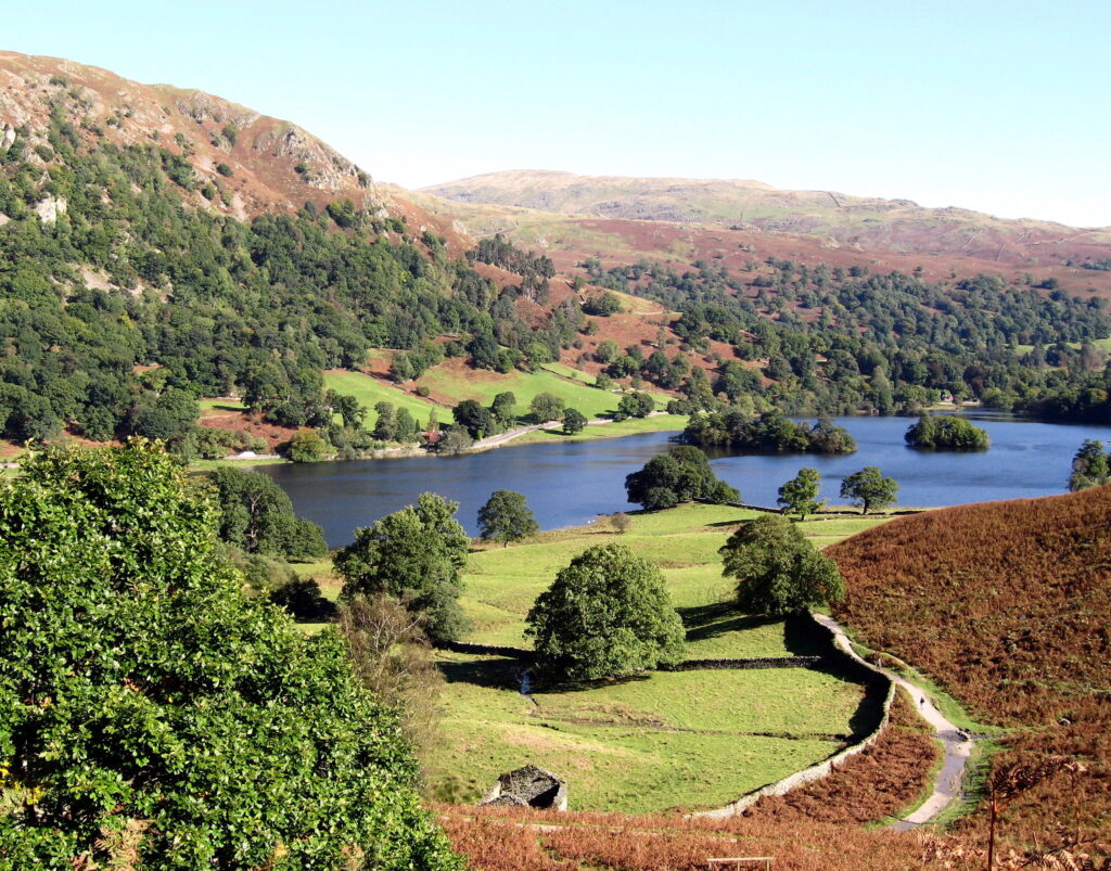 landscape view of rydal water surrounded by green fields, woodland and fells on a sunny day