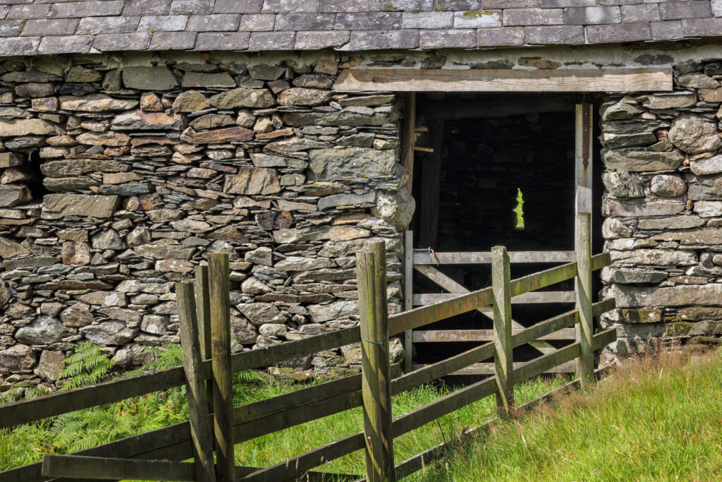 close up of stone barn with open door gap and wooden fence