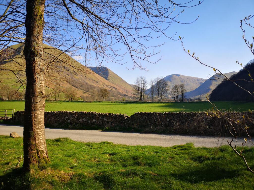 landscape view from cow bridge car park of green fields, dry stone wall, track and fells on a sunny day