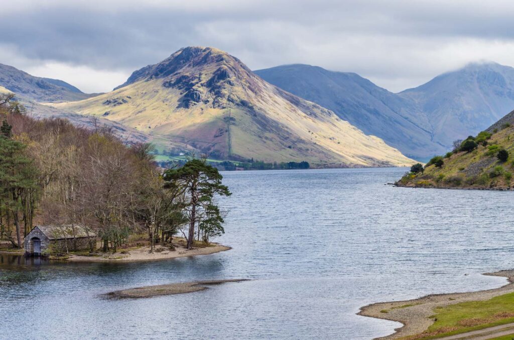 Wastwater with bare woodland and boathouse on the shore. Grey cloudy sky.