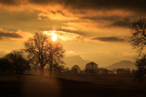 winter orange sunset at pooley bridge shadowing distant fells and close woodland