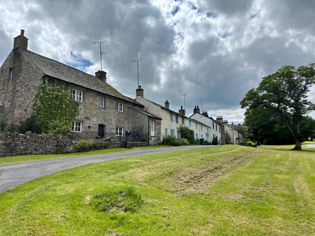 row of rural village houses made of stone, slate and limewash, with grass verge in front