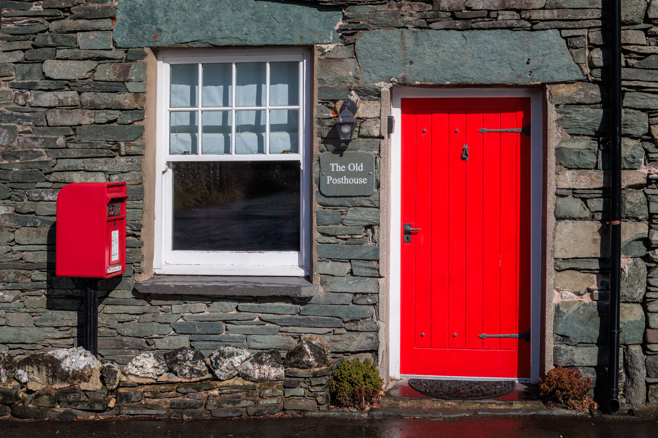 front exterior of slate building named the old post office. bright red door and post box with square window in the middle