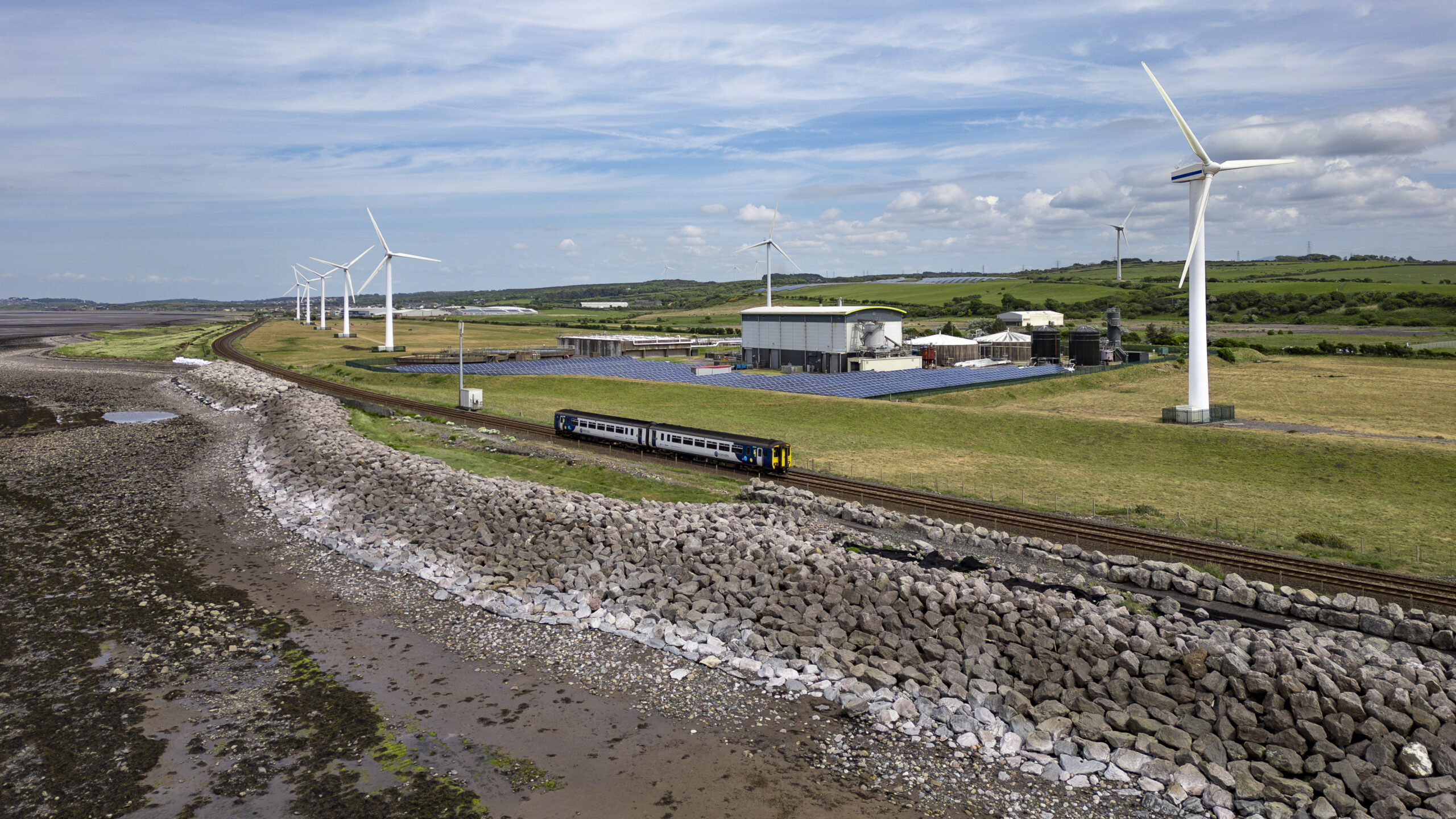 Wind turbines stood on field on side of a railway track