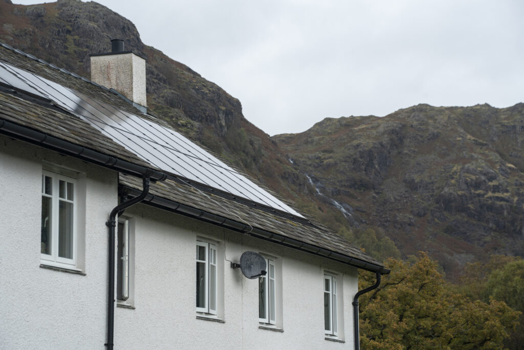 exterior top floor and roof of white house. roof is made of slate with solar panels. craggy fells in backdrop
