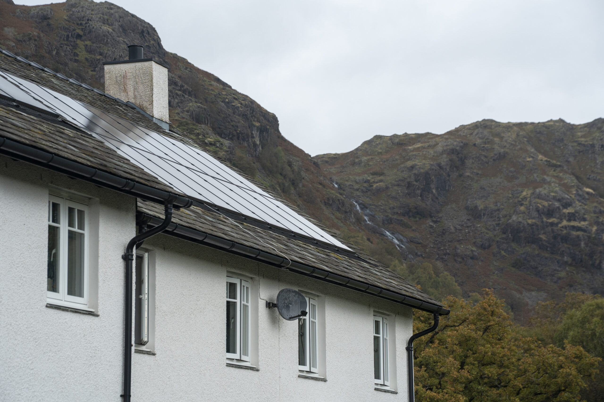 exterior top floor and roof of white house. roof is made of slate with solar panels. craggy fells in backdrop