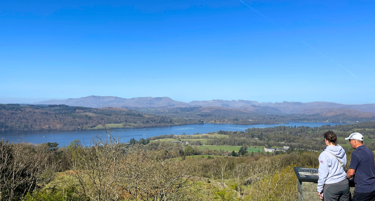 Panoramic view of Windermere from the summit of Orrest Head, two people stood at information board looking out