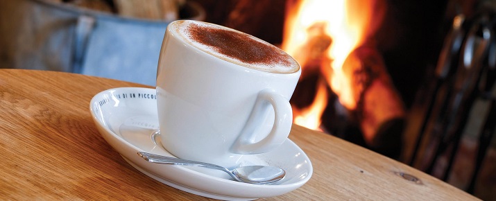 A big mug filled with hot chocolate next to a roaring fire