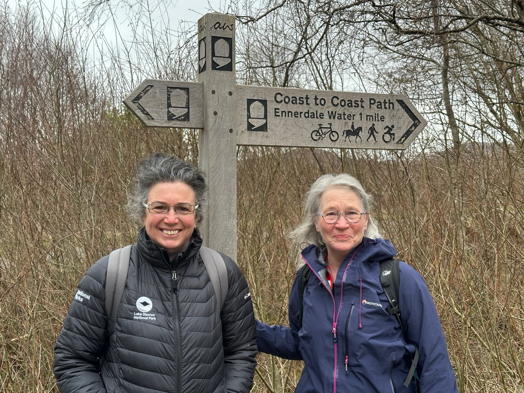 Two women standing next to wooden 'Coast to Coast' fingerpost