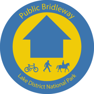 Blue waymarker roundel with yellow circle and blue arrow. Bike, person and horse symbol with text reading Public Bridleway
