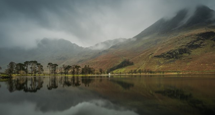 Fells towering over moody lake, reflecting in the water.