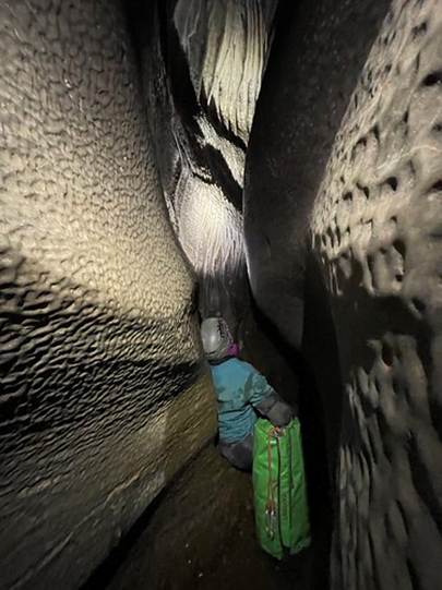 Person squeezing through tight gap in cave