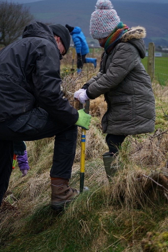 child being helped by ranger dig hole to plant tree