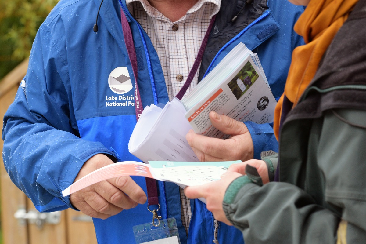 Close up image of someone in blue National Park unform showing a map to someone in a uniform. The image is cropped to the maps, hands and torsos of the two figures.