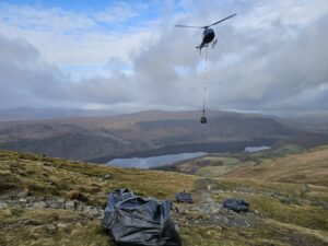 helicopter lifting bag of stones over landscape with lake in background