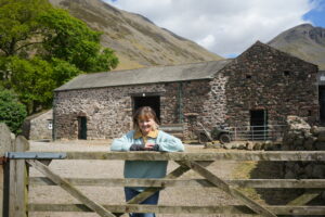 woman with her arms folded over the top of a wooden gate with a stone building behind