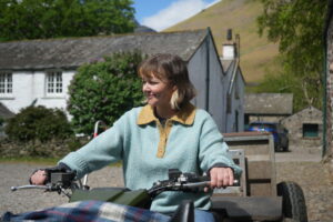 Woman riding a quad bike on a sunny day outside a farmhouse