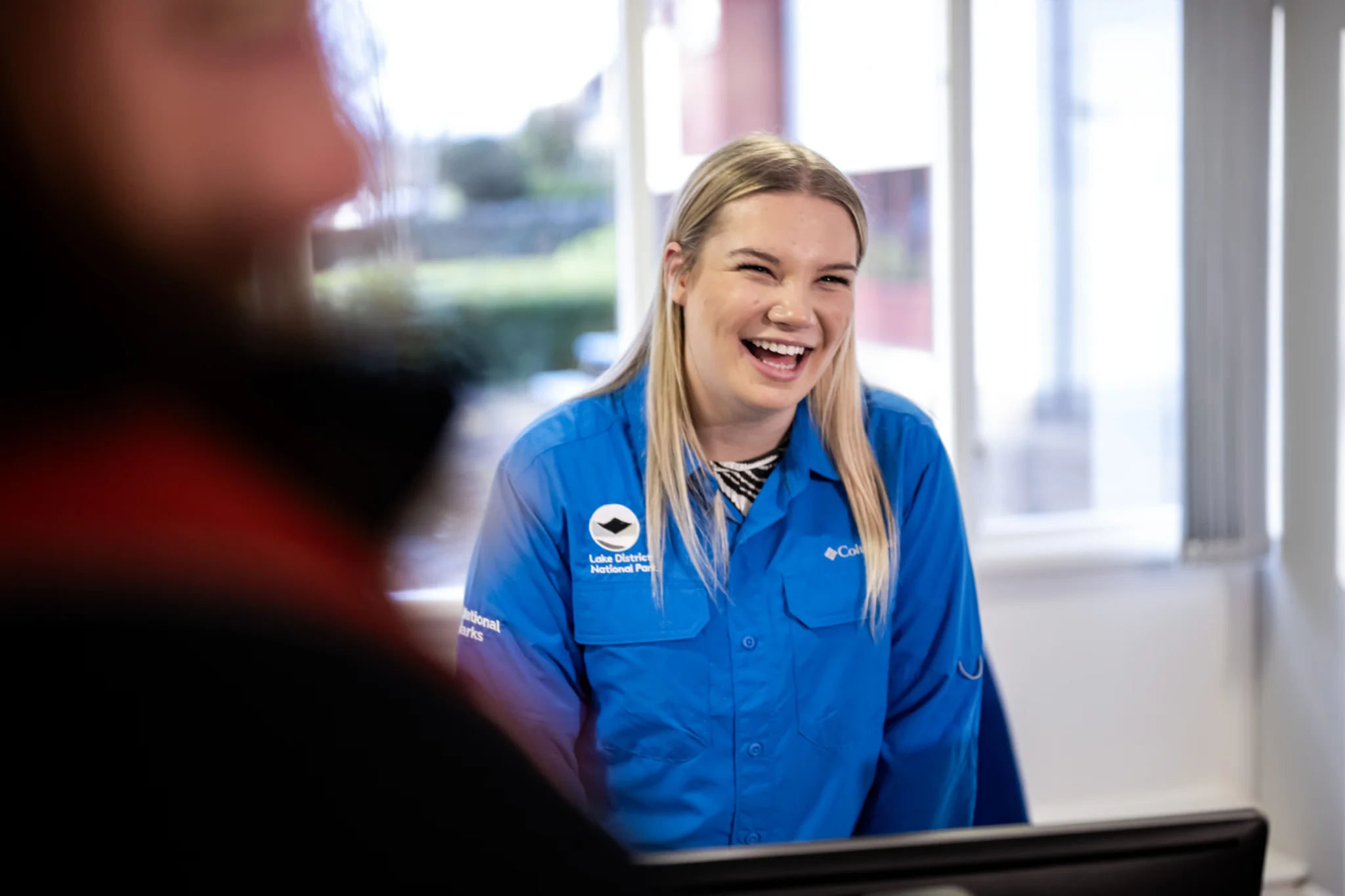 A colleague in blue branded shirt with a huge grin welcoming