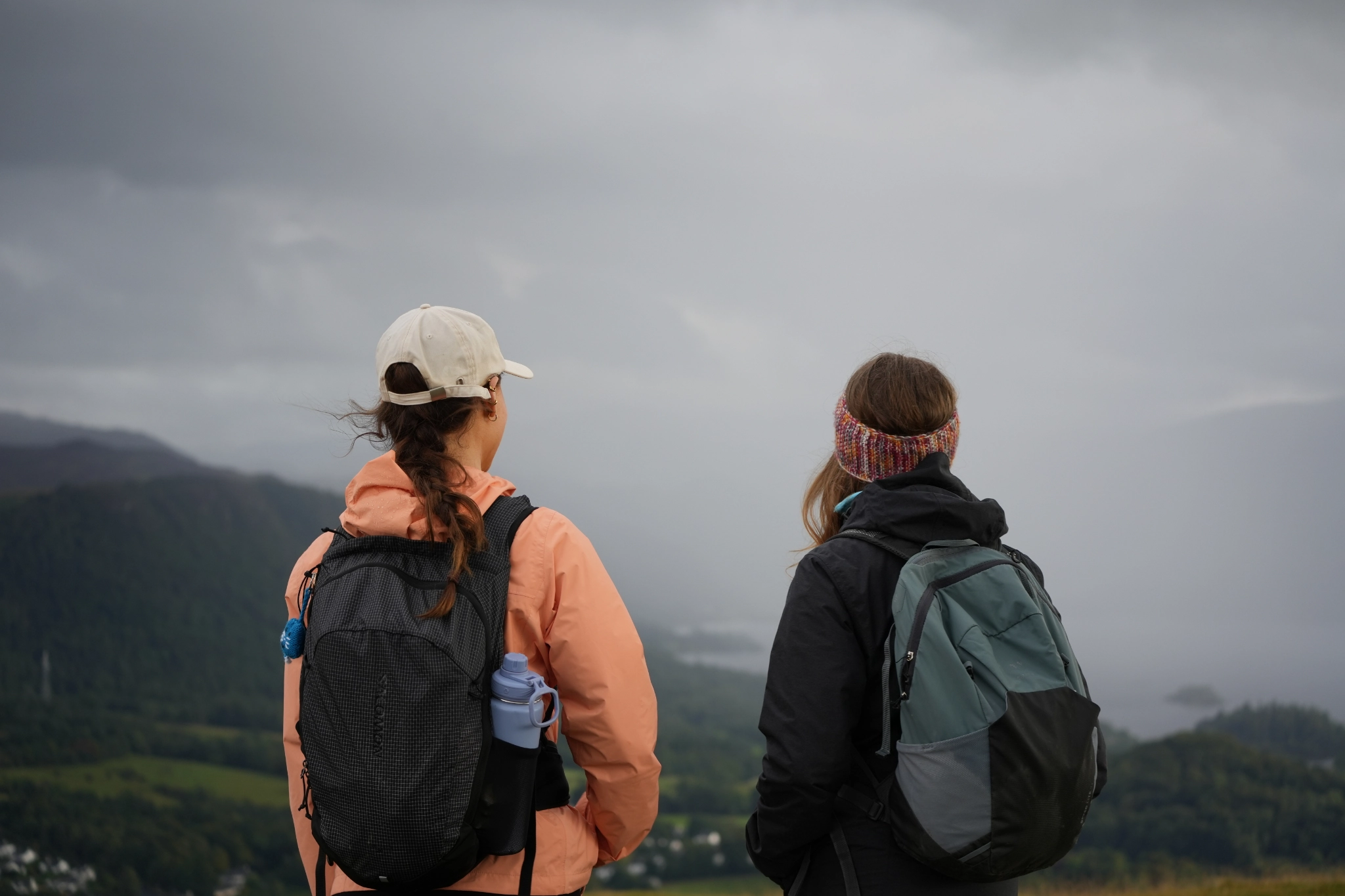 two young women facing away from camera looking out to misty fells in outdoor walking gear